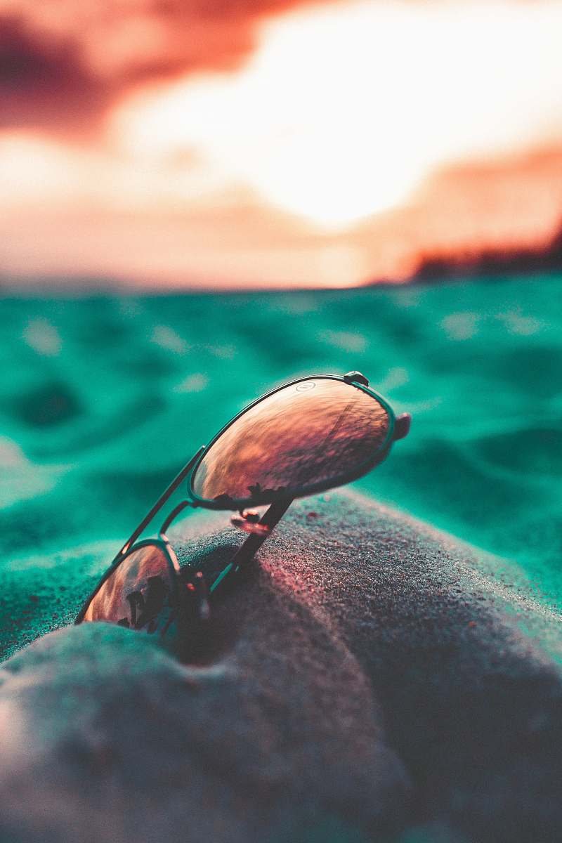 sunglasses close up photography of black Aviator-style sunglasses on gray sand naples